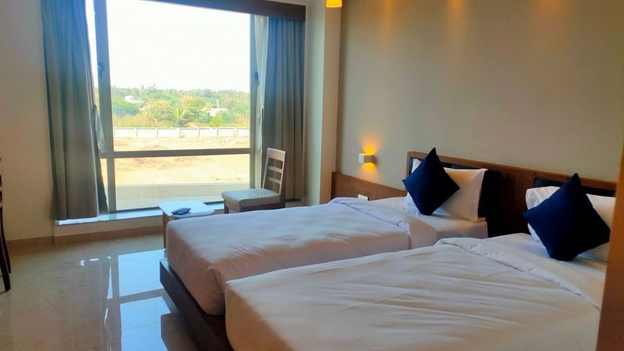 An image of our room displaying twin beds with cozy pillows, a neat environment, relaxing furniture to stretch out, and a window