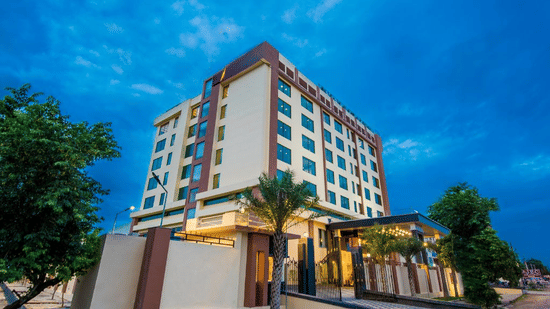 An angled evening view of a contemporary hotel building illuminated against a twilight sky, featuring a paved driveway and greenery at Golden Tulip Kukas, Jaipur.