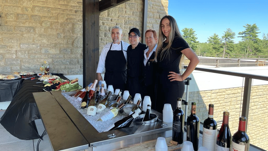 Four chefs and a woman stand behind a table with food and wine bottles with their backs towards a balcony at YO1 Longevity & Health Resorts, Catskills