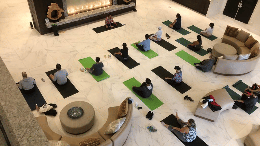 A group of people practice yoga on mats in a spacious indoor area with a fireplace and modern furniture at YO1 Longevity & Health Resorts