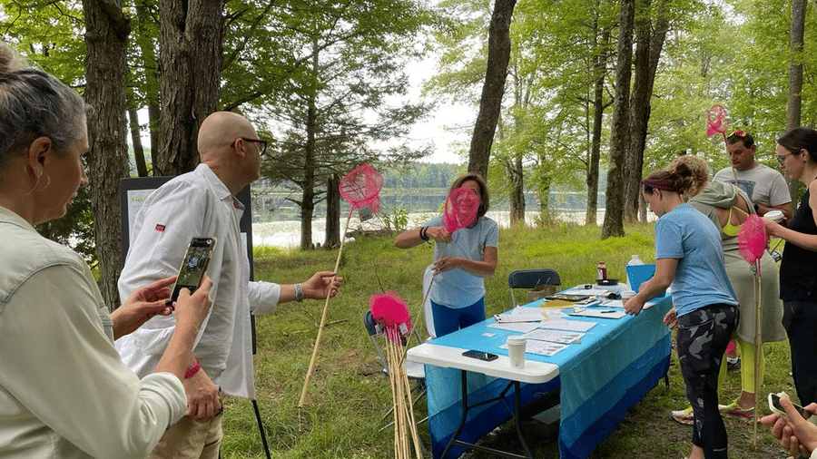 A group of people outdoors holding pink butterfly nets, gathered around a table with a person talking at YO1 Longevity & Health Resorts, Catskills