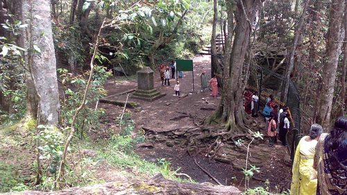 Exterior of Guna Caves near kodaikanal with many trees, a pathway and people in view.