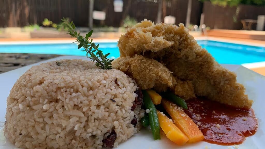 A plate with rice and a piece of fried fish or chicken, served by a swimming pool | Altamont Court, Jamaica