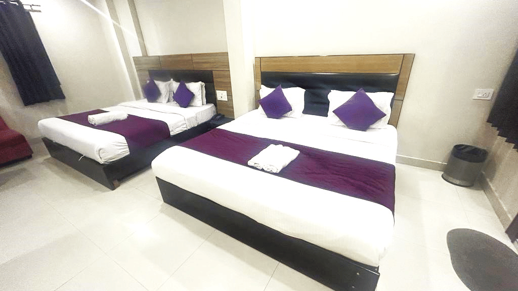 Interior view of a hotel room with one double bed and one single bed at Perfectstayz Value Dwarkesh, Haridwar.