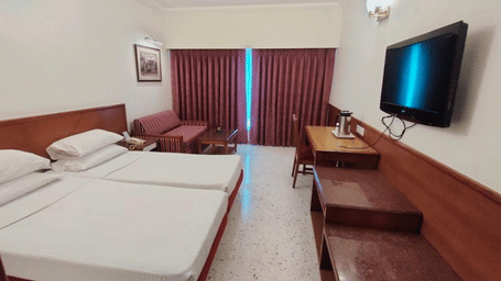 A hotel room featuring twin beds, a wall-mounted flat-screen television, a wooden desk with a chair, and red curtains | Trance Oakwood Hotel, Pune