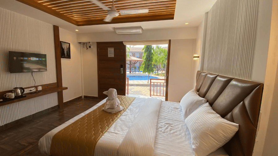 Modern guest room view showing a wall-mounted TV, wooden rafters on the ceiling, and direct access to the pool area - DAN Resorts & Weddings, Palghar