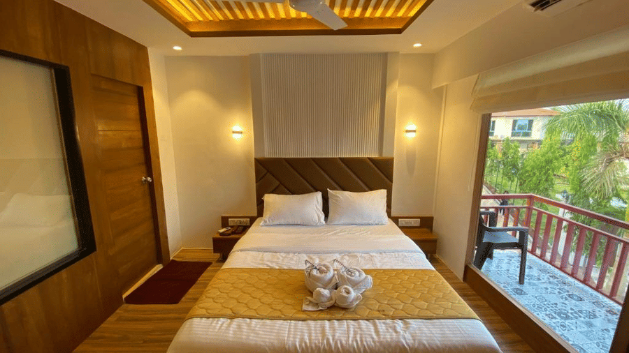 Well-lit luxury room featuring a king size bed and large glass doors leading to a private wooden balcony - DAN Resorts & Weddings, Palghar