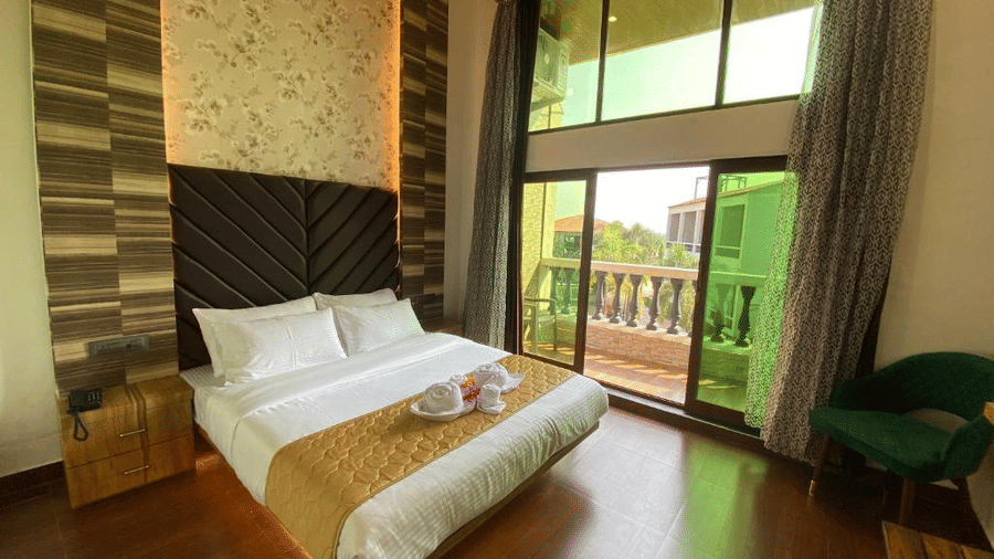 High-ceiling guest room with polished wooden floors, warm lighting, and floor-to-ceiling balcony windows - DAN Resorts & Weddings, Palghar