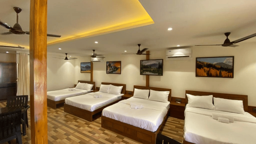 Spacious group accommodation featuring four double beds, wooden flooring, and warm recessed ceiling lighting - DAN Resorts & Weddings, Palghar
