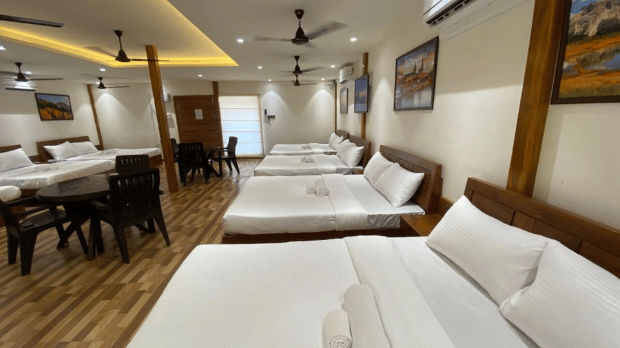 Long guest room with multiple double beds and a central dining table for group stays - DAN Resorts & Weddings, Palghar