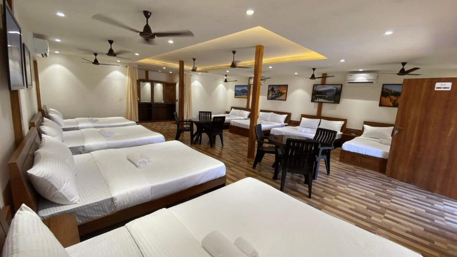 Interior view of a large family room showing row of beds and a wooden wardrobe unit - DAN Resorts & Weddings, Palghar