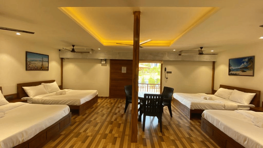 Large open-plan guest room with multiple beds, wooden accents, and an central architectural pillar - DAN Resorts & Weddings, Palghar