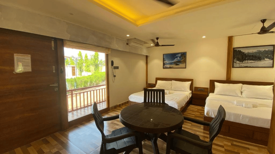 Guest room featuring two double beds and a small dining set with natural light from a balcony door - DAN Resorts & Weddings, Palghar