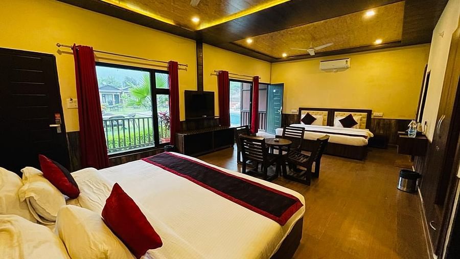 A Family Cottage with beds facing towards each other seperated by a round dining table and TV at DLS MJ River Resort, Rishikesh.