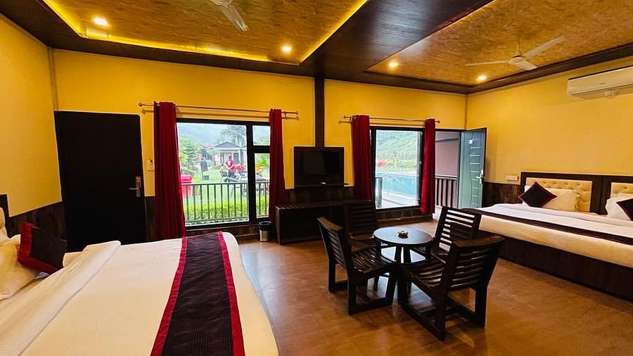 View of the dining table placed in front of a TV with outdoor views on either sides in Family Cottage at DLS MJ River Resort, Rishikesh.