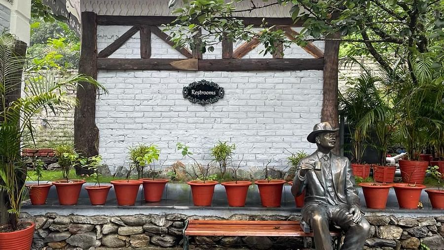 A sidewalk bordered by potted plants and small trees, with a metal statue enhancing the area
