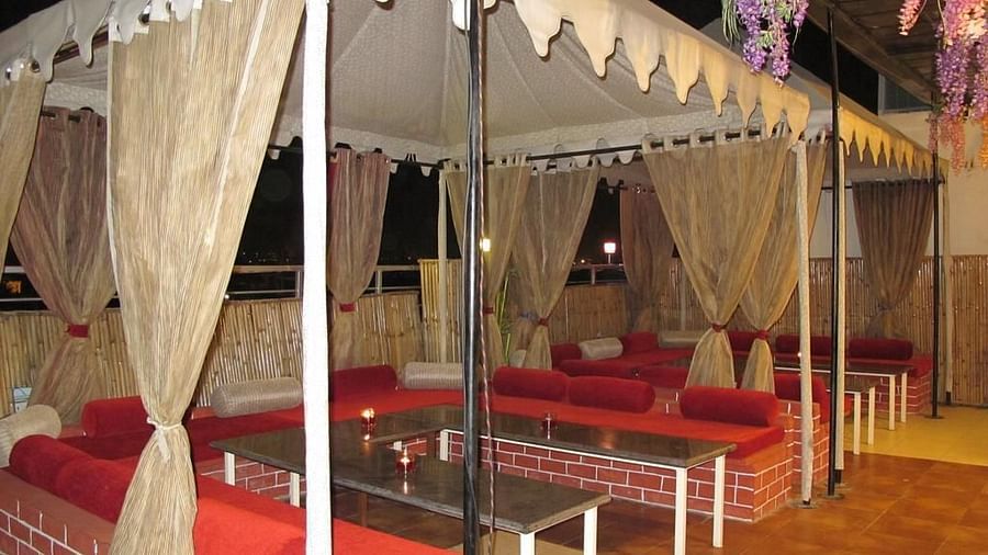 An open-air cabana with sheer curtains, red cushions on bench seating and a view of the city at night - TGI Apple Inn, Jaipur 