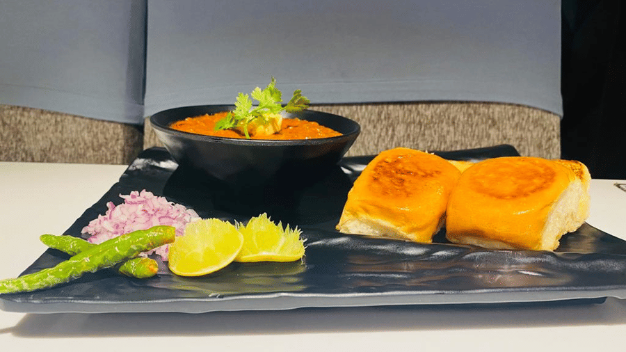 Pav bhaji at The Citrine, Bangalore, with a black bowl of red bhaji, toasted pav, chopped onion, green chilli, and lemon on a black tray.