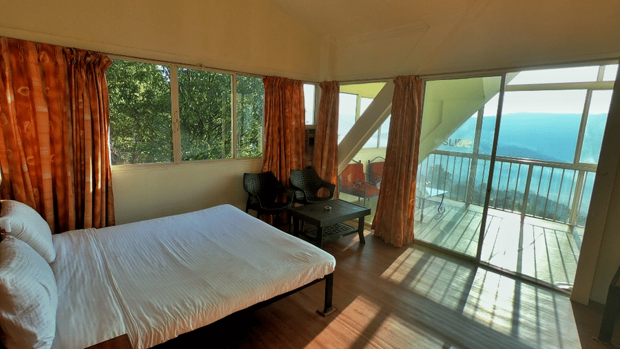 A spacious room with a large bed, a wooden table and chair in the corner, and a large balcony offering a view of nature at Wind Chalet Resort.