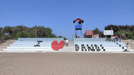 A wide shot of a beach with a monument that says, 'I love DANDI'.