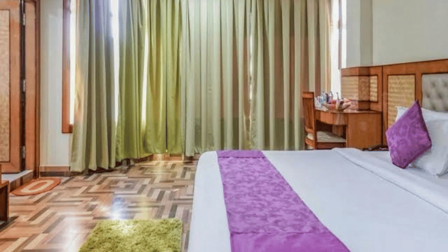 A spacious bedroom with rich wooden flooring, green drapes, and a purple-accented bed for a cosy stay at Pemaling Lords Eco Inn Guwahati.
