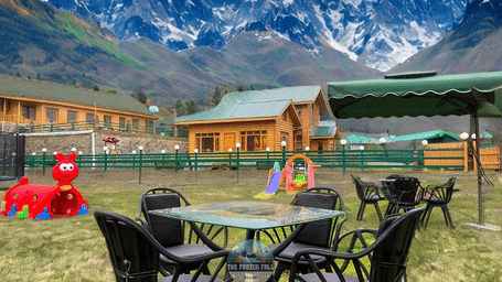 A lawn seating area at Dawat e Drung by FrozenFall Resort, Drung, Tangmarg, with 1 table, 4 chairs, children's play equipment and mountains.