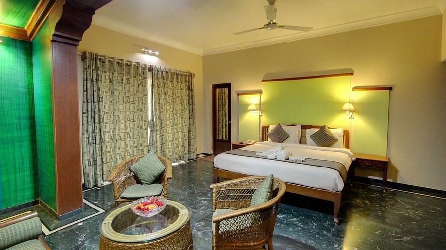 A well-lit room at Damanganga Valley Resorts in Silvassa featuring a plush bed and a sitting space in front of it including a coffee table and couches