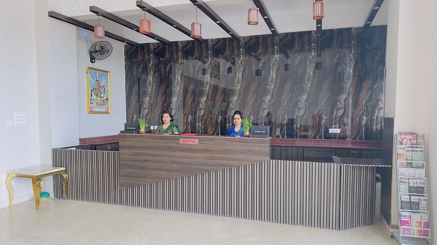 A reception desk with a striped front and wooden accents is shown with staff members - Kankidham Lords Inn