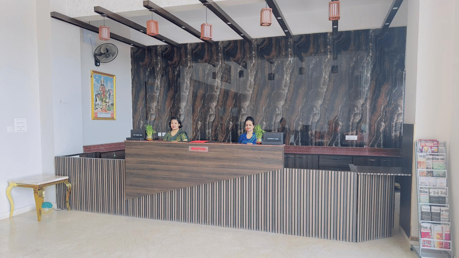 A reception desk with a striped front and wooden accents is shown with staff members - Kankidham Lords Inn