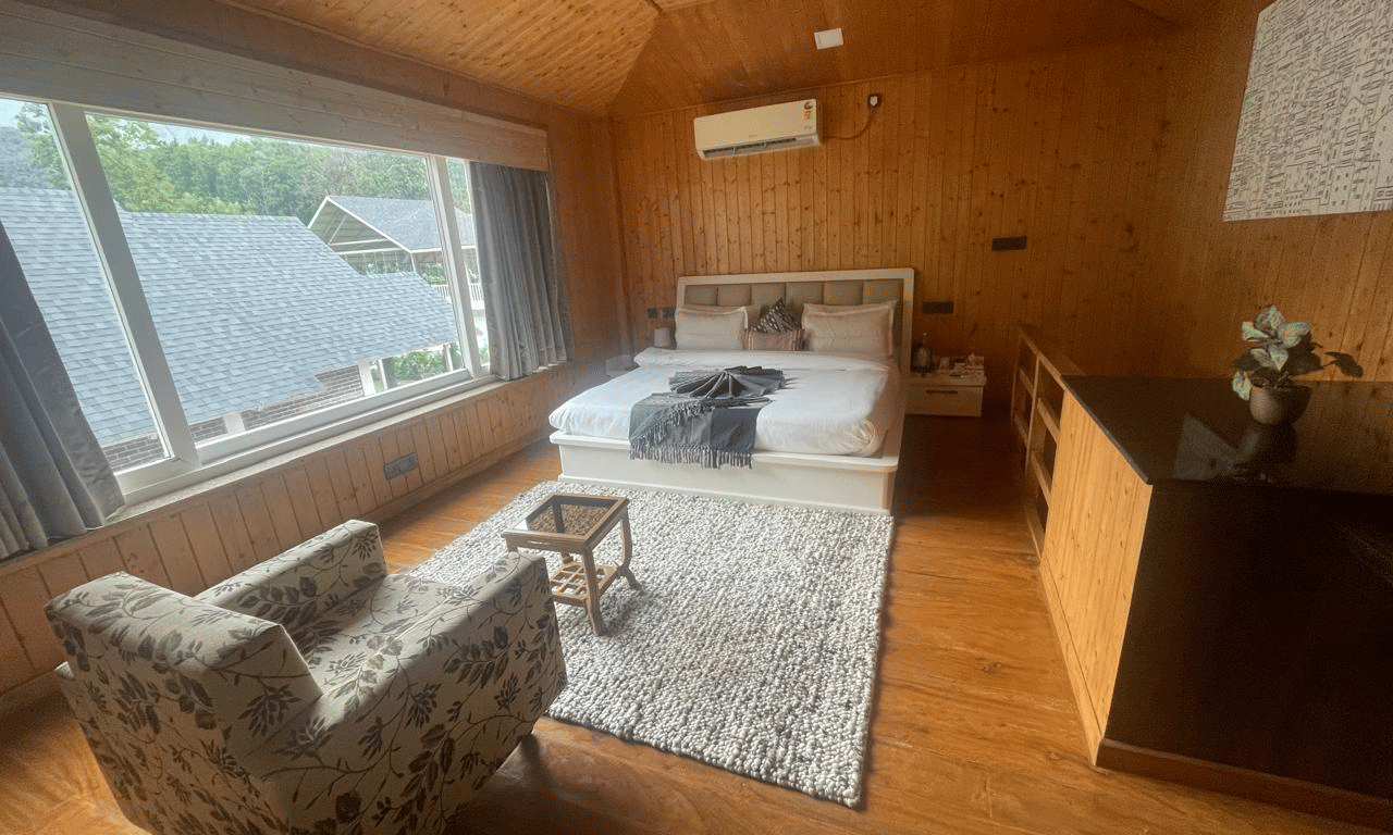 An angled shot of a bedroom with large windows, a comfortable chair, and a white rug at Megha Resort & Villas, Dehradun.