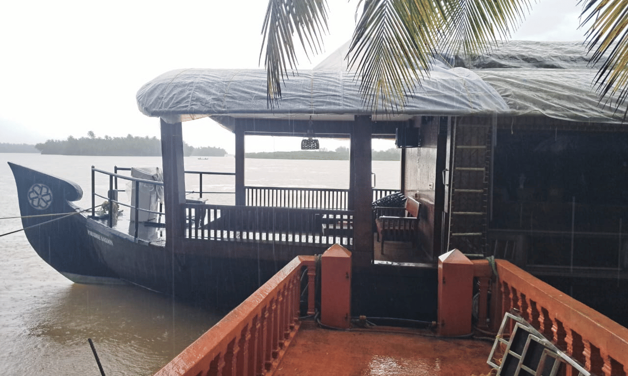 Traditional style wooden houseboat docked near a palm tree at Paradise Lagoon Resort, Udupi.