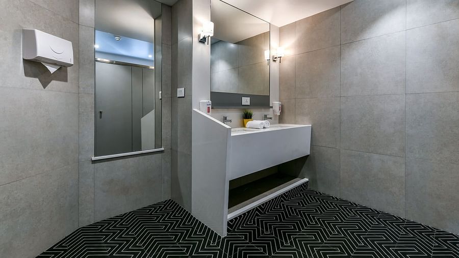 A washroom with a portrait and mirror, a landscape mirror above the washbasin, wall-mounted tissue box, and essentials like hand wash and rolled towels on the counter at Indie Stays, BKC Kalina.