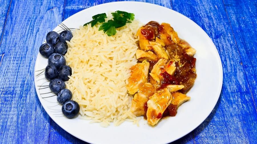A white plate holds a serving of rice, with meat, and blueberries, presented on a blue textured surface | Altamont Court, Jamaica