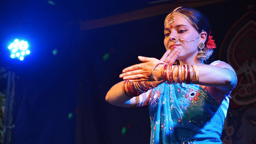 a classical Indian dancer dancing on a stage with a spotlight in the background