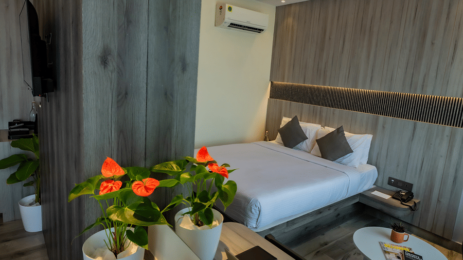 Hotel bedroom with a king size bed, floral arrangement, bedside tables, wooden wall panelling and a wall-mounted air conditioner.