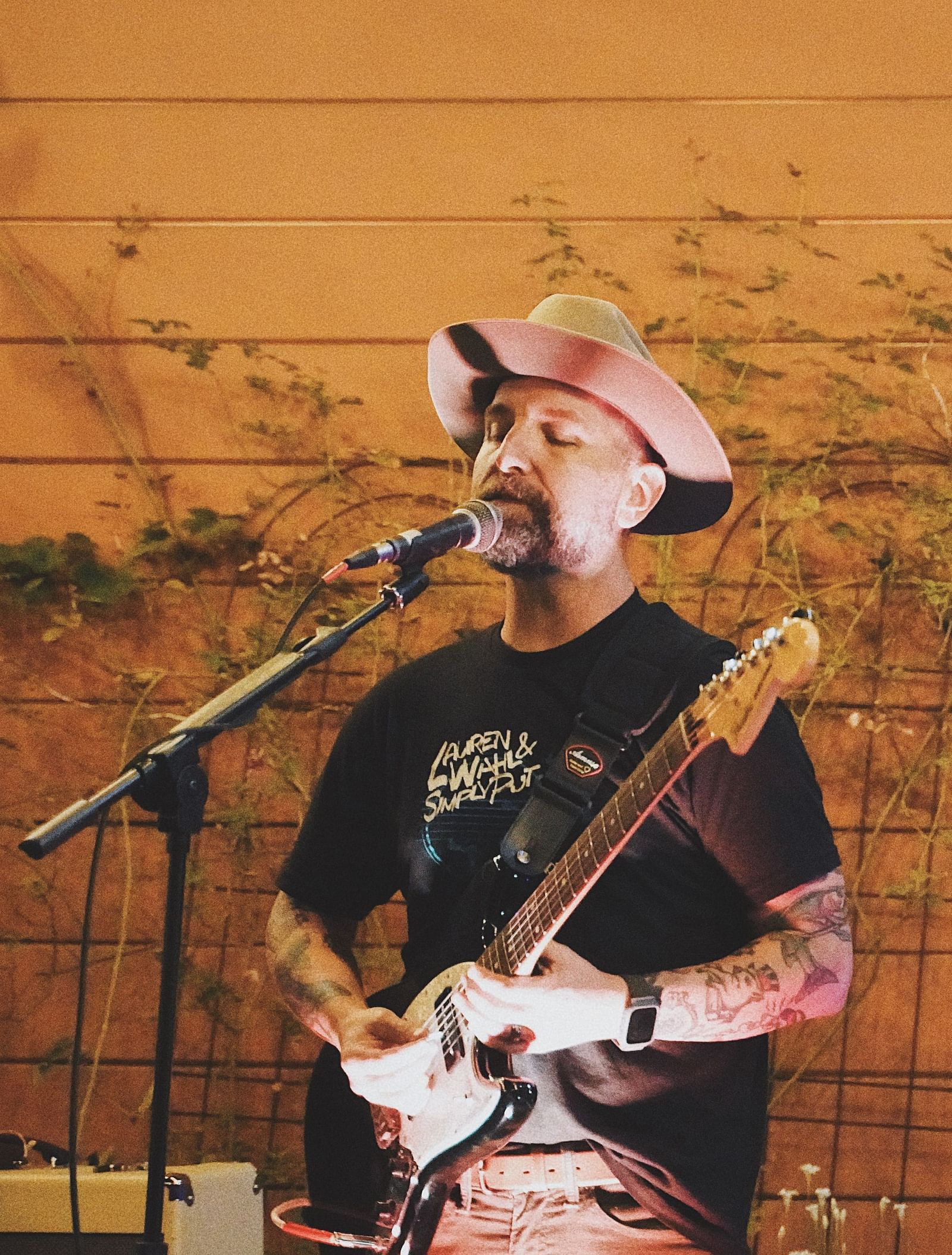 A person with a hat singing while playing the guitar - The Groveland Hotel.