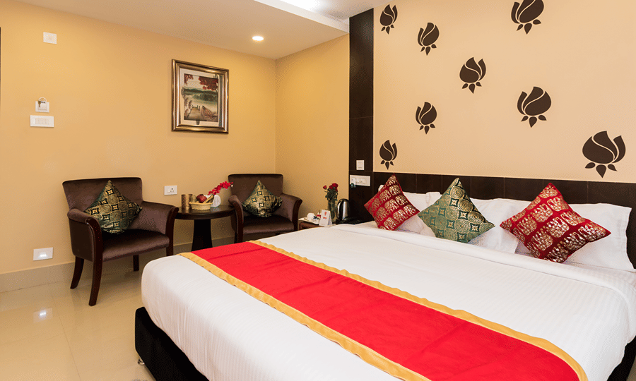 One of the hotel rooms in Siliguri at Central Courtyard Boutique Hotel featuring plush bed against a wall with floral patterns and a seating space for 2 next to it