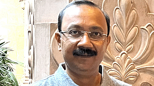 Bijitendra Mittra in a grey polo shirt standing in front of a carved stone wall, smiling at the camera.