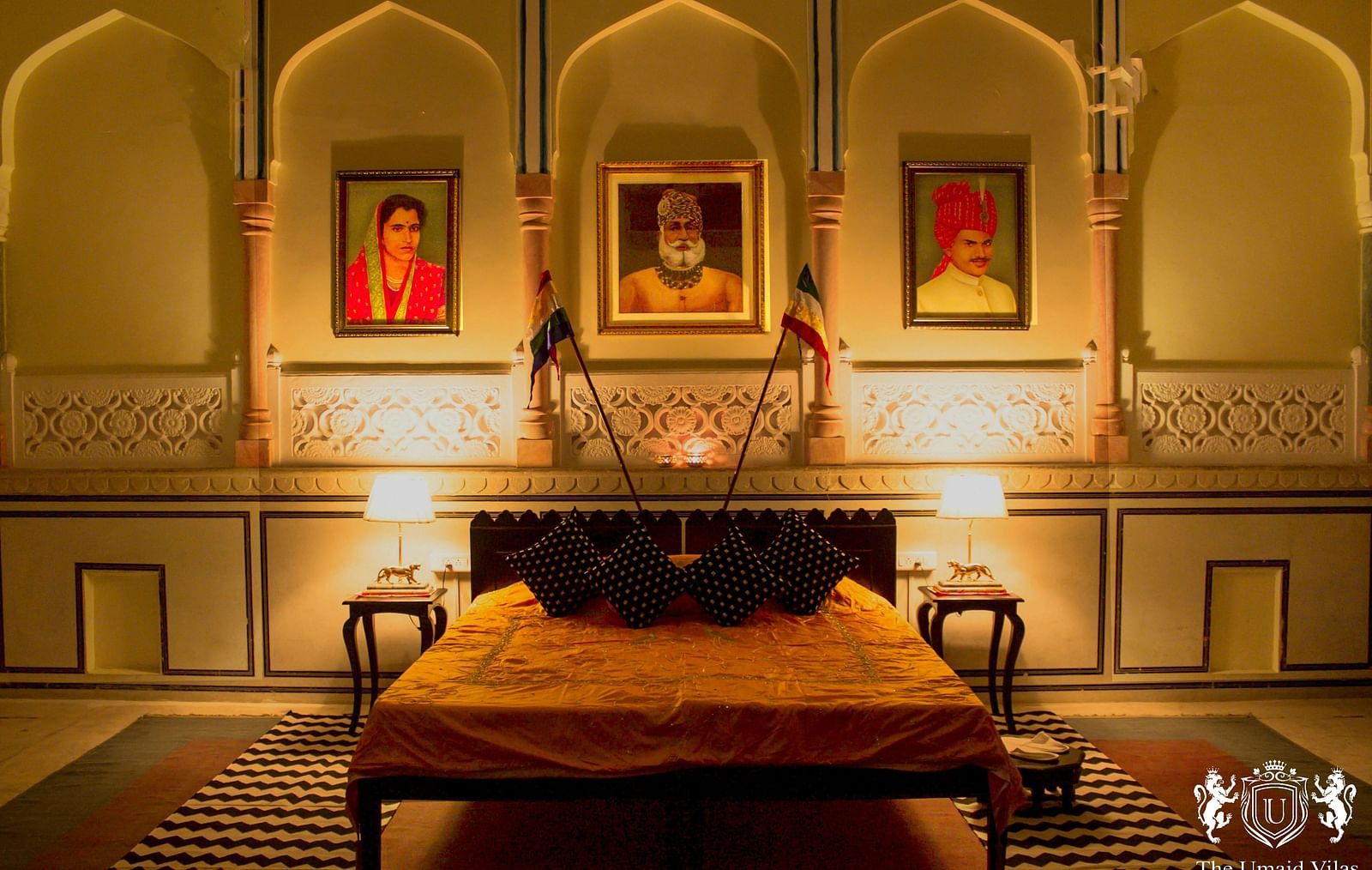 A bedroom at Umaid Vilas Jaipur with a low bed, framed portraits, and arched alcoves in the walls.