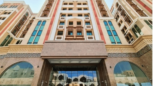 Facade view of La Maison Hotel, Doha from below with blue sky in the background.