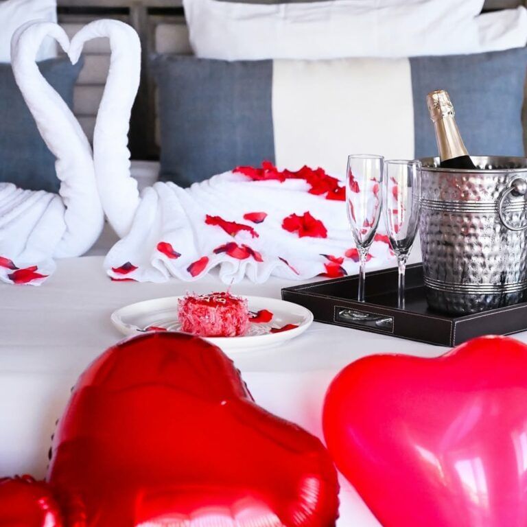 A bed decorated with swan-shaped towels, red heart pillows, and rose petals, suggesting a romantic setting.