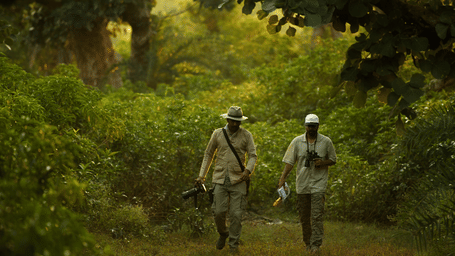 An image two men walking amidst green a forest - An image of a jeep parked amidst the rocky mountains - Utsav Camp Sariska