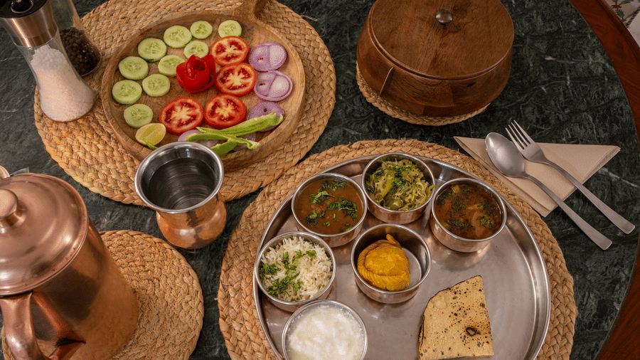 Overhead view of a food spread served on wooden boards on a round dark table at Barwara Kothi, Jaipur.