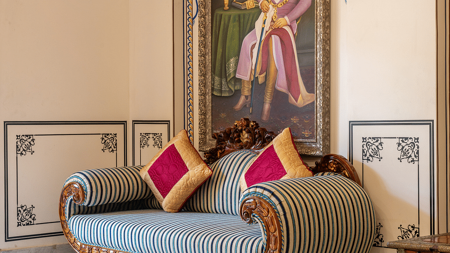 corner view image of a comfortable vintage couch with two cushions kept over it along with a huge portrait of a maharaj - Brij Castle, Jaipur