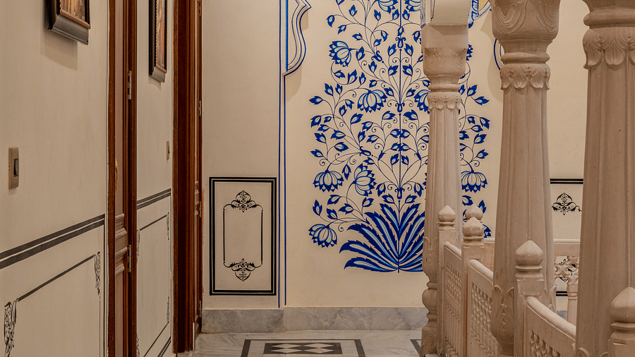 a corridor with blue floral patterns painted in the wall at the far end with beautiful pillars in the side - Brij Castle, Jaipur