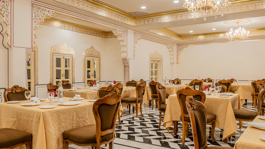 a brightly lit dining area with ample space to walk besides the beige table cloth cover dining tables - Brij Castle, Jaipur