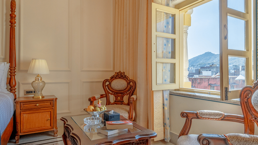 two beautiful wooden armchairs placed in front of a coffee table with open windows - Brij Castle, Jaipur