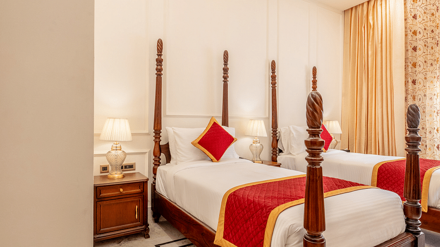 a bedroom with elegant interiors featuring a false ceiling along with a twin bed with bed sides tables beside it - Brij Castle, Jaipur