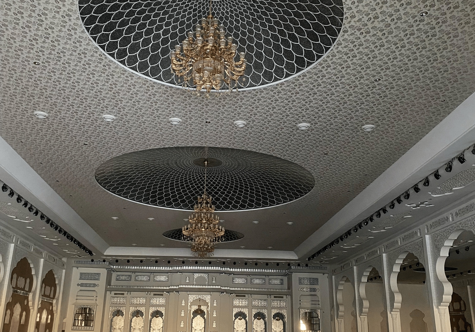 Large banquet hall with chandeliers, ornate ceiling and round dining tables at Beelwa Palace, Jaipur