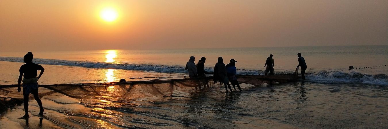 Silhouettes of people on beach at sunrise with golden sun reflecting on wet sand and calm sea